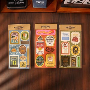 May include: Three sticker sheets with vintage-style designs. The sheets feature various illustrations, including a fox, a can of food, and travel-themed graphics. Each sheet has a brown header with the "BENSTORE" logo and text.