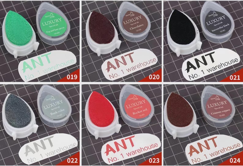 May include: A collection of six ink pads in various colors, including green, brown, black, gray, and red. Each pad is in a white teardrop-shaped holder with a clear lid. The text "ANT No. 1 warehouse" is visible.