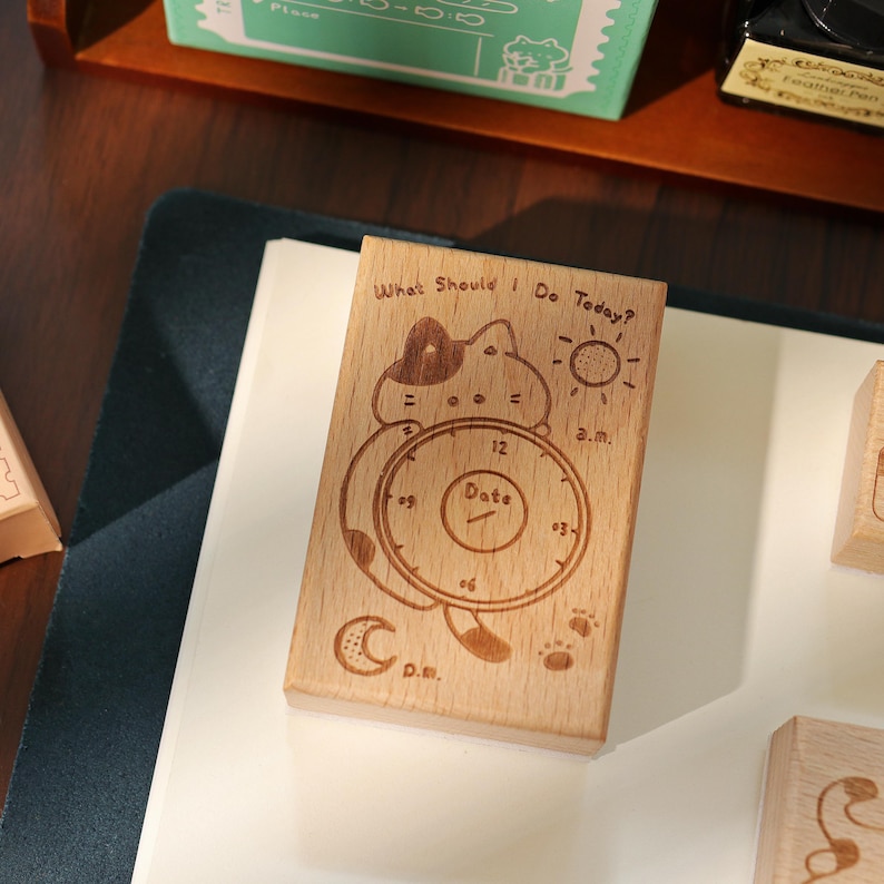 May include: Wooden stamp with a cat design and the text "What Should I Do Today?" The stamp includes a clock face with "Date" in the center, a sun, a moon, and paw prints. The stamp is made of light-colored wood.