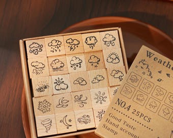 May include: A set of 25 wooden stamps featuring weather-related illustrations, including clouds, rain, sun, and wind. The stamps are arranged in a box with a brown paper label that reads "Weather".