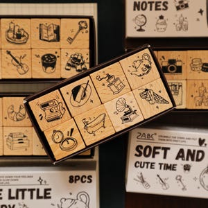 May include: Wooden stamp sets with various black and white illustrations, including a key, a violin, a coffee cup, and a slice of cake. The stamps are arranged in boxes, with the text "SOFT AND CUTE TIME" visible on one box.