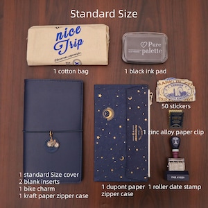 Op de afbeelding: Een verzameling briefpapierartikelen, waaronder een marineblauw notitieboek met een fietsbedel, een katoenen tas met de tekst "nice Trip", een zwart inktkussen, stickers en een roldatumstempel. De items liggen op een houten oppervlak.