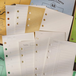 Könnte beinhalten: Verschiedene A5-Planer-Papier-Nachfüllungen mit Raster-, Linien- und To-Do-Listen-Formaten. Das Papier ist weiß und cremefarben, mit vorgestanzten Löchern zum Binden. Einige Blätter haben Text.