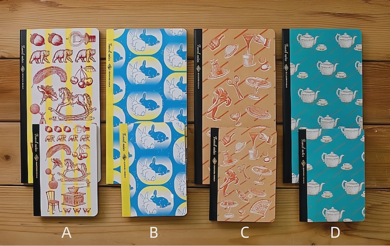 May include: Four notebooks with different cover designs. One has a yellow background with illustrations of bears, cherries, and a rocking horse. Another has a blue background with white rabbits. The third has a tan background with food illustrations. The last has a teal background with teapots.