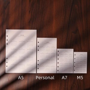 May include: Four white 2026 yearly planner inserts in A5, Personal, A7, and M5 sizes. Each insert has a calendar grid layout with the year printed at the top. The inserts have pre-punched holes for binding.