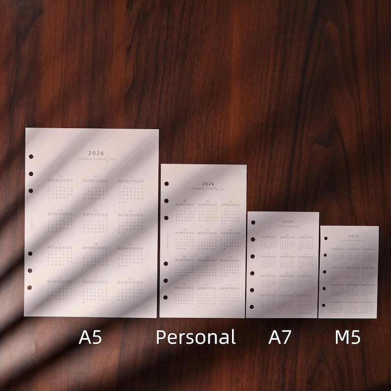 May include: Four white 2026 yearly planner inserts in A5, Personal, A7, and M5 sizes. Each insert has a calendar grid layout with the year printed at the top. The inserts have pre-punched holes for binding.