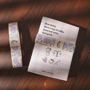 May include: A white and lavender patterned bookmark and a folded card with text and illustrations. The bookmark features a floral design and a small rabbit graphic. The card reads "Slow down. Have a cup of coffee. Read and write. Feel good."
