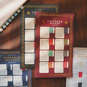 May include: A collection of calendar stickers with various designs and dates. The stickers feature months from 2025, 2026, and 2027, with a burgundy, navy blue, and black background. Each sticker has a decorative border and the words "CALENDAR STICKER".