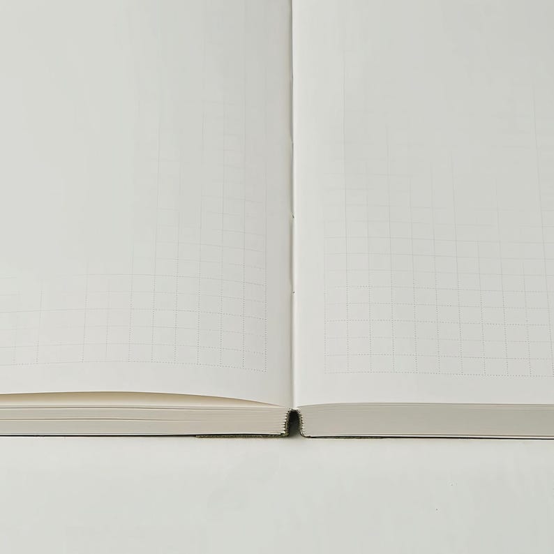May include: Open notebook with grid-lined pages. The pages are white with a subtle grid pattern, perfect for writing or sketching. The notebook is open, revealing the inner pages and the binding.