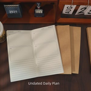 May include: An open notebook with a daily plan layout, featuring lined pages and boxes for AM and PM entries. The text "Undated Daily Plan" is at the bottom. Several brown paper covers are visible to the right. A small calendar shows the year 2025.