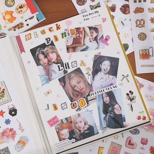 May include: A scrapbook page featuring photographs of the K-pop group Blackpink, including members Lisa and Jisoo. The page is decorated with various stickers, including hearts, stars, ribbons, and text cutouts that spell out Blackpink, Lisa, and Jisoo.