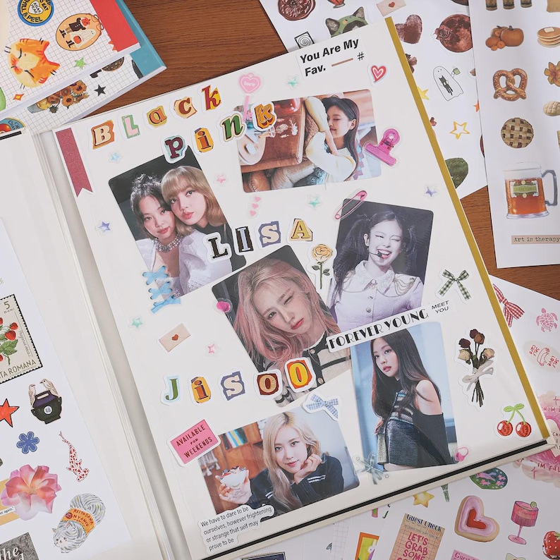 May include: A scrapbook page featuring photographs of the K-pop group Blackpink, including members Lisa and Jisoo. The page is decorated with various stickers, including hearts, stars, ribbons, and text cutouts that spell out Blackpink, Lisa, and Jisoo.