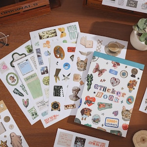 May include: A sticker book with a grid-patterned cover featuring the text Sticker Book and 1300+ stickers, surrounded by multiple loose sticker sheets displaying various illustrations including cats, butterflies, flowers, and vintage-style graphics.