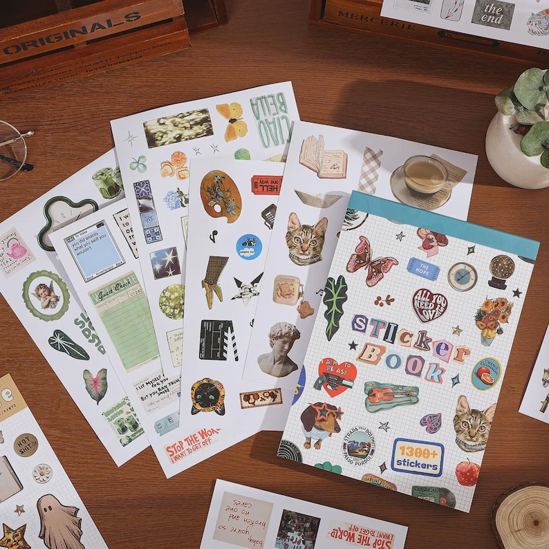 May include: A sticker book with a grid-patterned cover featuring the text Sticker Book and 1300+ stickers, surrounded by multiple loose sticker sheets displaying various illustrations including cats, butterflies, flowers, and vintage-style graphics.