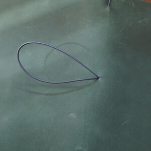 May include: A dark teal leather surface with a dark blue elastic loop. The loop is in the shape of a teardrop. The leather has a subtle texture and slight variations in color.