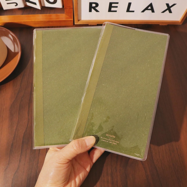 May include: Two olive green notebooks in clear plastic covers. The notebooks have a vertical olive green stripe down the left side. The word "Relax" is visible in white block letters in the background.