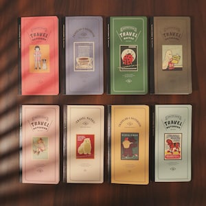 Könnte beinhalten: Acht Notizbücher mit farbenfrohen Einbänden werden gezeigt. Jedes Notizbuch trägt die Aufschrift "TRAVEL NOTEBOOK" und eine einzigartige Illustration im Vintage-Stil. Die Einbände sind in Rot, Blau, Grün, Braun, Rosa, Creme, Gelb und Hellblau gehalten.