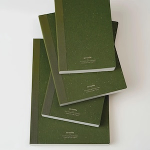 May include: Four green notebooks of varying sizes are stacked on top of each other. The notebooks have a textured cover and a spine in a slightly darker shade of green. The text "WriteMe" is printed on the bottom right corner of each notebook.