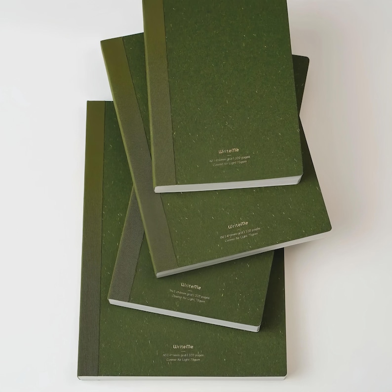 May include: Four green notebooks of varying sizes are stacked on top of each other. The notebooks have a textured cover and a spine in a slightly darker shade of green. The text "WriteMe" is printed on the bottom right corner of each notebook.