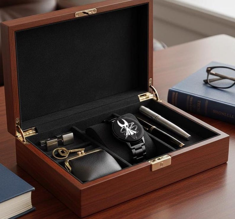 Puede incluir: Una caja de reloj de madera oscura, abierta para revelar un interior negro con un reloj negro con un dise&ntilde;o blanco, bol&iacute;grafos, un peque&ntilde;o monedero y otros accesorios. La caja est&aacute; sobre una superficie de madera.