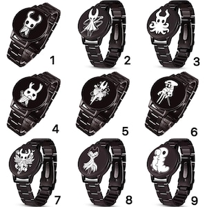 Puede incluir: Una colecci&oacute;n de nueve relojes de pulsera negros con varios dise&ntilde;os de personajes blancos en las esferas. Los relojes tienen correas de metal negro y esferas redondas. Cada reloj presenta una ilustraci&oacute;n de personaje diferente.