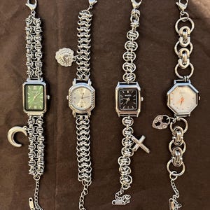 May include: Four silver-toned wristwatches with various face shapes and chain-link bands. The watch faces are green, silver, black, and white. Each watch has a different charm, including a crescent moon, a heart, and a cross.