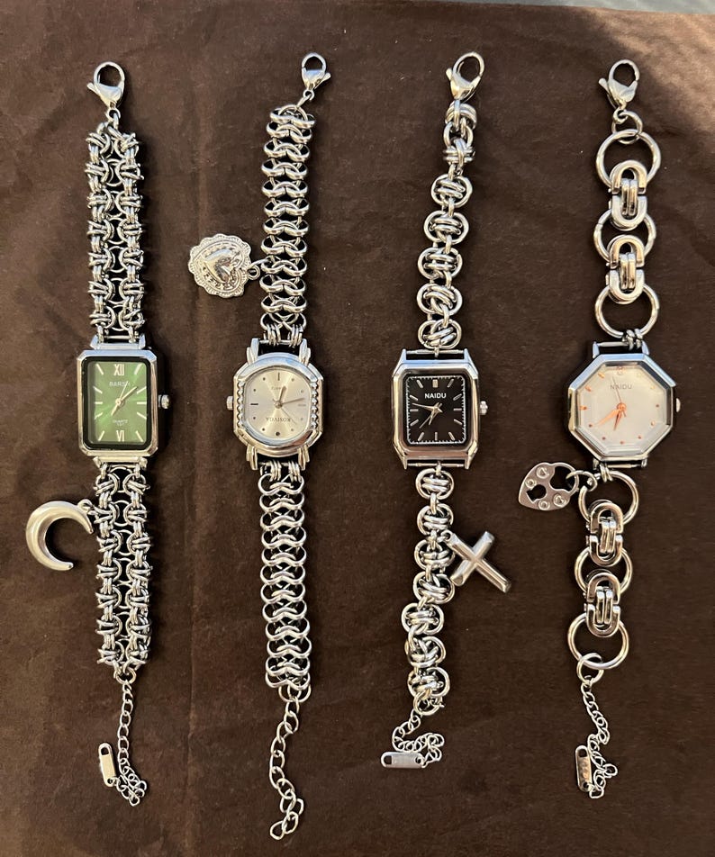 May include: Four silver-toned wristwatches with various face shapes and chain-link bands. The watch faces are green, silver, black, and white. Each watch has a different charm, including a crescent moon, a heart, and a cross.