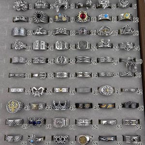 Puede incluir: Un expositor lleno de sesenta anillos plateados. Los anillos presentan varios diseños, incluyendo motivos animales, patrones geométricos y detalles ornamentados. Algunos anillos tienen acentos de piedras de colores. Los anillos están dispuestos en una cuadrícula.