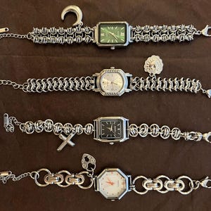 May include: Four silver-toned watches with unique chain-link bands and watch faces. One watch has a green face, another has a black face, and a third has a white face. A silver-toned ear gauge and a charm are also present.