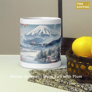 May include: White ceramic mug featuring a watercolor illustration of Mount Fuji in winter. The design includes a snowy landscape, trees, and the text "Japanese Winter". The mug has a wraparound design.