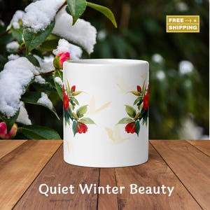 Puede incluir: Taza de cerámica blanca con un diseño floral de flores rojas y hojas verdes. La taza tiene un patrón repetido de siluetas de pájaros amarillos. El texto "Quiet Winter Beauty" está en la parte inferior.