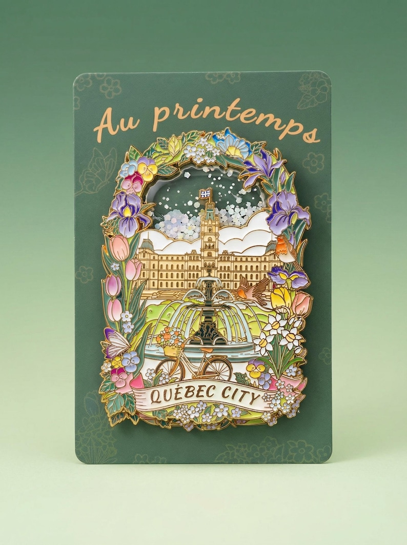 May include: A decorative pin featuring a colorful illustration of Quebec City, with a floral border and the words "Au printemps" and "Quebec City". The pin includes a bicycle, fountain, and building.
