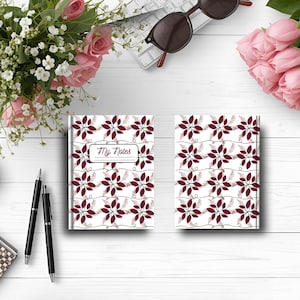 Può includere: Due quaderni con sfondo bianco e un motivo di fiori bordeaux e steli verdi. I quaderni hanno il testo "My Notes" in una cornice rettangolare. L'immagine include anche penne, fiori e occhiali da sole.
