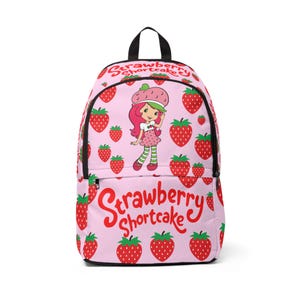 May include: A light pink backpack featuring a repeating strawberry pattern and a central illustration of the character Strawberry Shortcake. The text Strawberry Shortcake is printed in red at the top and bottom of the bag, which has black zippers.