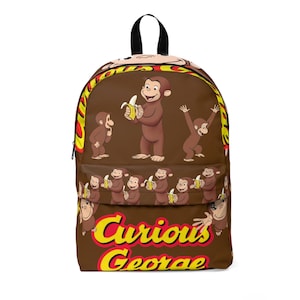 May include: A brown backpack with illustrations of Curious George. The backpack has a black handle and zip. The design includes Curious George with bananas and the words "Curious George" in yellow and red.