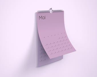 Op de afbeelding: Een lila wandkalender met een zilveren spiraalbinding hangt tegen een bijpassende muur. Het woord "Mai" staat bovenaan gedrukt. De pagina is gedeeltelijk omgeslagen en toont de kalender.