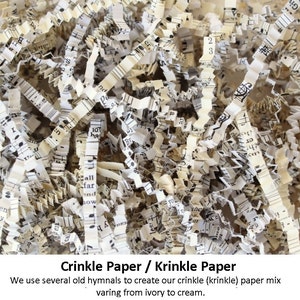 Close-up of white and cream crinkle paper made from old hymnals. The paper is shredded and has black musical notes printed on it. The text 'Crinkle Paper / Krinkle Paper' is at the top of the image. The text 'We use several old hymnals to create our crinkle (krinkle) paper mix varing from ivory to cream.' is at the bottom of the image.