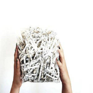 A white plastic bag filled with shredded white paper with black musical notes printed on it.