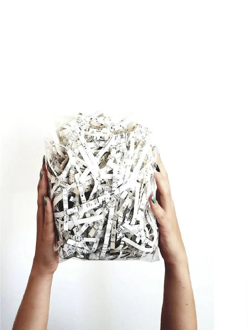 A white plastic bag filled with shredded white paper with black musical notes printed on it.