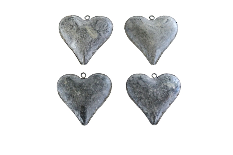 May include: Four heart-shaped pendants made of a grey, textured metal material. Each heart features a smooth, rounded surface with a mottled, weathered appearance and a small metal loop attached to the top center for hanging or attachment purposes.