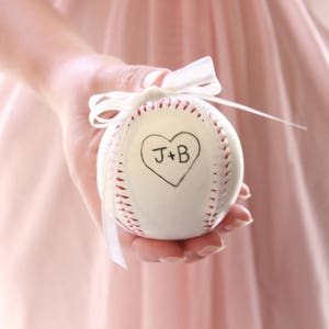 A white baseball with with a white bow to tie rings to for a baseball themed wedding.