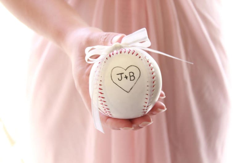 A white baseball with with a white bow to tie rings to for a baseball themed wedding.