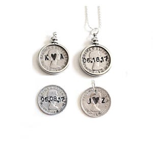 May include: Four silver coin pendants with personalized engravings. Two pendants have initials and a heart, one with a date. One pendant hangs from a silver chain. The pendants are on a white background.