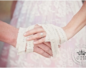 May include: A close-up of two hands holding each other, with a white fabric ribbon wrapped around their wrists. The ribbon has the words "I love you" printed on it. The woman's hand is wearing a diamond engagement ring.