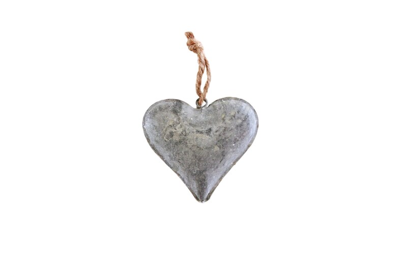 May include: A heart-shaped ornament made of weathered gray metal with a textured, mottled surface. The heart features a small metal loop at the top, which is attached to a short, twisted piece of natural brown jute twine for hanging purposes.