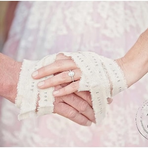 May include: A close-up of two hands holding a piece of white fabric with the words "I love you" written on it. The fabric is tied around the hands, and a diamond ring is on the finger of one hand.