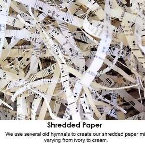 A close-up image of shredded paper made from old hymnals. The paper is a mix of ivory and cream colors. The paper is shredded into thin strips and has musical notes printed on it. The text 'Shredded Paper' is printed below the image. The text 'We use several old hymnals to create our shredded paper mix varying from ivory to cream.' is printed below the text 'Shredded Paper'.