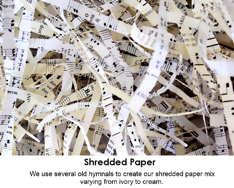 A close-up image of shredded paper made from old hymnals. The paper is a mix of ivory and cream colors. The paper is shredded into thin strips and has musical notes printed on it. The text 'Shredded Paper' is printed below the image. The text 'We use several old hymnals to create our shredded paper mix varying from ivory to cream.' is printed below the text 'Shredded Paper'.