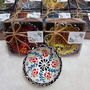 Op de afbeelding: Handbeschilderde keramische kommen met ingewikkelde bloemmotieven in rood, blauw en geel. Elke kom is verpakt in een doorzichtige doos en vastgebonden met touw. De kommen hebben een geschulpte rand en een zwarte rand.