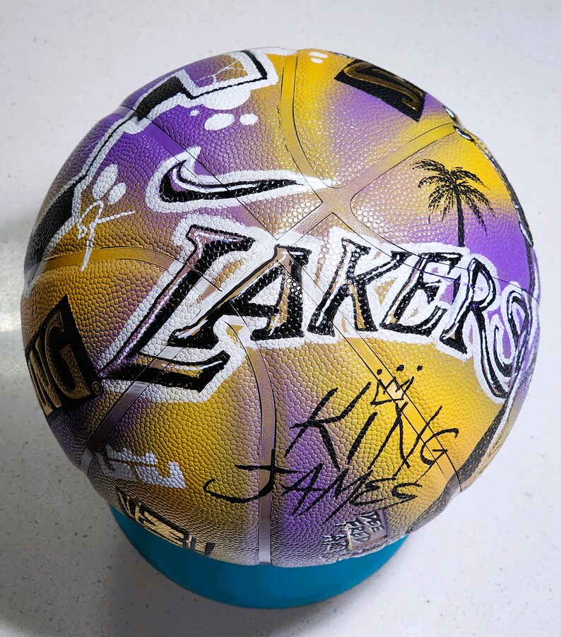 May include: A basketball in the colours yellow, purple, and white, with the word "Lakers" in large letters. The Nike logo, a palm tree, and the words "King James" are also visible on the ball's surface.